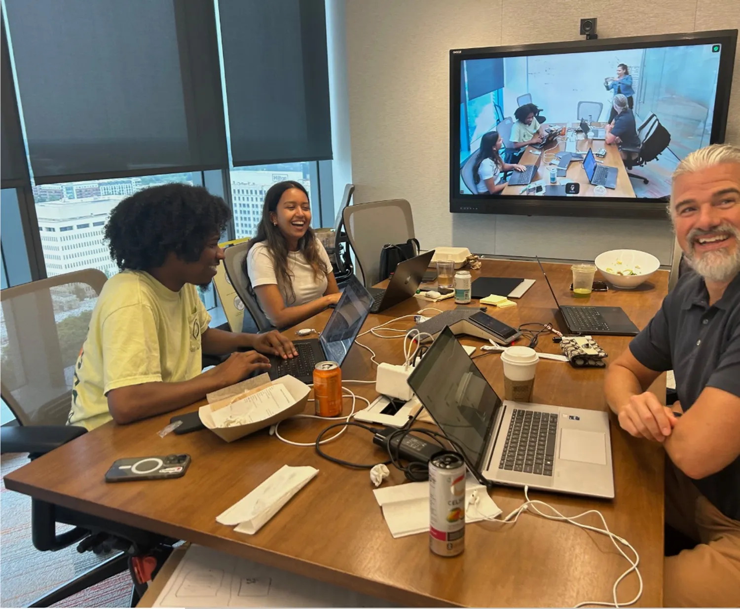 The cross-functional team working together in a conference room during the in-person venture sprint, with a remote teammate on screen